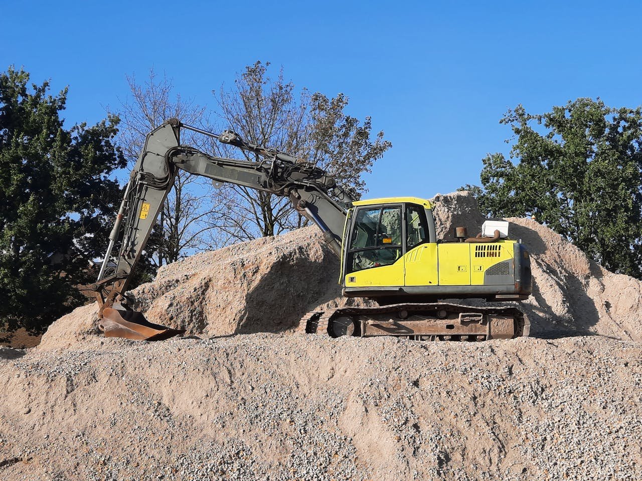 About A yellow excavator working on a gravel mound at a construction site.